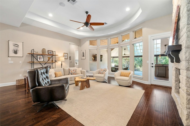 living room featuring ceiling fan, dark wood-type flooring, a tray ceiling, and a fireplace