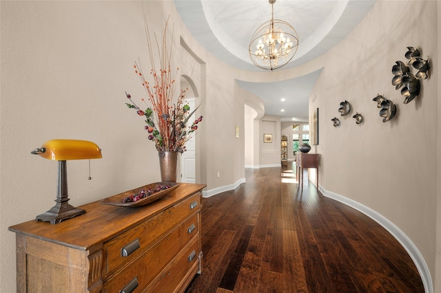 corridor featuring dark hardwood / wood-style flooring, a raised ceiling, and an inviting chandelier