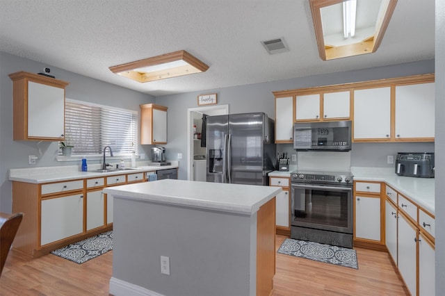 kitchen featuring a textured ceiling, a center island, white cabinetry, stainless steel appliances, and sink