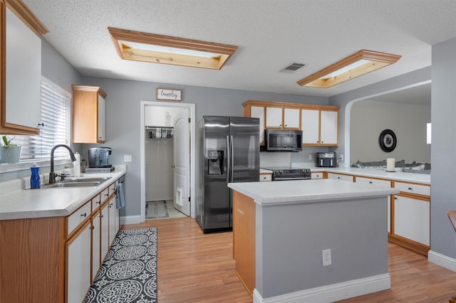 kitchen featuring appliances with stainless steel finishes, a textured ceiling, sink, a kitchen island, and light wood-type flooring