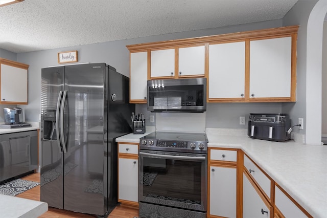 kitchen with white cabinetry, light hardwood / wood-style flooring, stainless steel appliances, and a textured ceiling