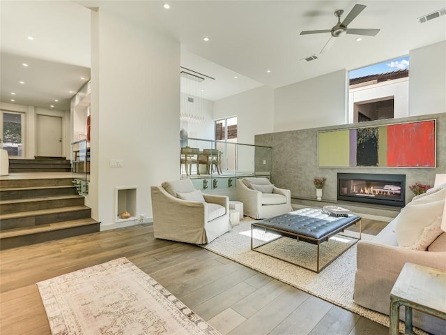 living room featuring stairway, visible vents, wood finished floors, and a glass covered fireplace