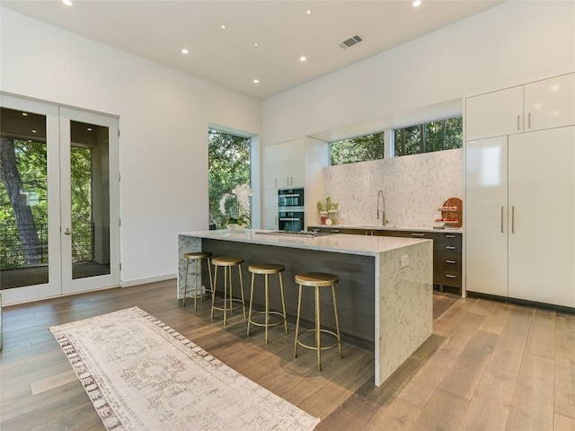 bar featuring light wood-style floors, tasteful backsplash, visible vents, and a sink