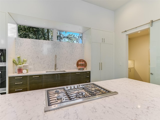 kitchen featuring sink, white cabinetry, a barn door, and stainless steel gas stovetop