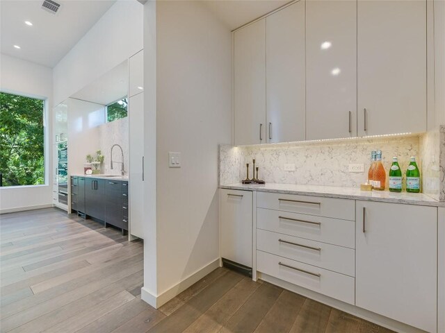 bar with light stone countertops, white cabinetry, sink, backsplash, and light wood-type flooring