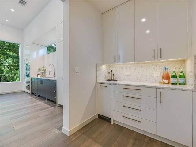 bar featuring light wood finished floors, tasteful backsplash, a sink, and visible vents