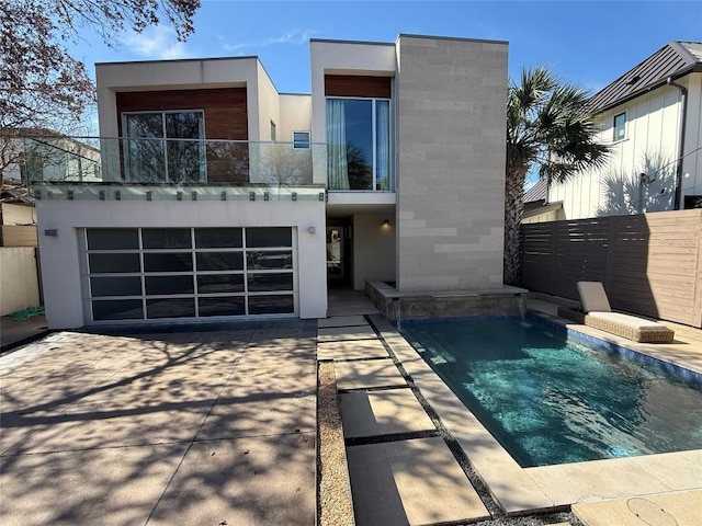 view of front of home featuring stucco siding, fence, a balcony, a garage, and driveway