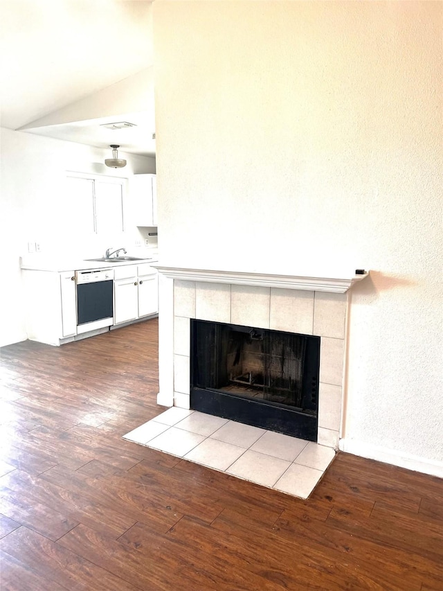 room details featuring sink, hardwood / wood-style floors, black dishwasher, and a tiled fireplace