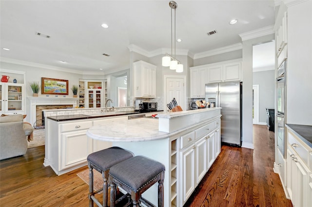 kitchen featuring appliances with stainless steel finishes, white cabinets, a kitchen island, sink, and hanging light fixtures