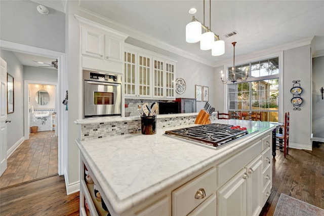 kitchen with ceiling fan with notable chandelier, a center island, stainless steel appliances, ornamental molding, and light stone counters