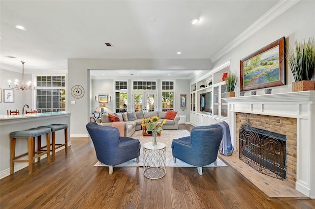 living room with crown molding, a brick fireplace, built in shelves, dark hardwood / wood-style floors, and a chandelier