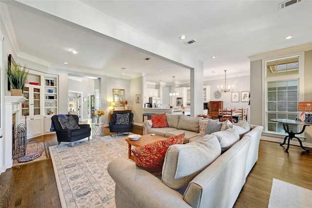 living room with built in features, hardwood / wood-style flooring, a notable chandelier, and ornamental molding