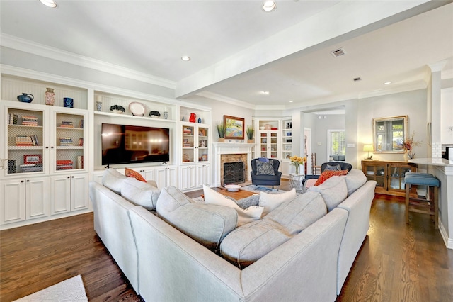 living room featuring built in features, dark hardwood / wood-style flooring, crown molding, and a fireplace