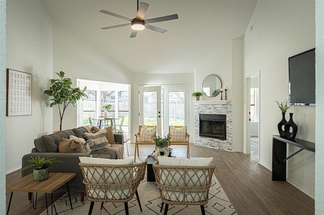 living room with hardwood / wood-style flooring, ceiling fan, high vaulted ceiling, and a stone fireplace