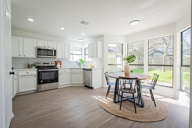 kitchen with white cabinetry, stainless steel appliances, sink, backsplash, and light hardwood / wood-style flooring