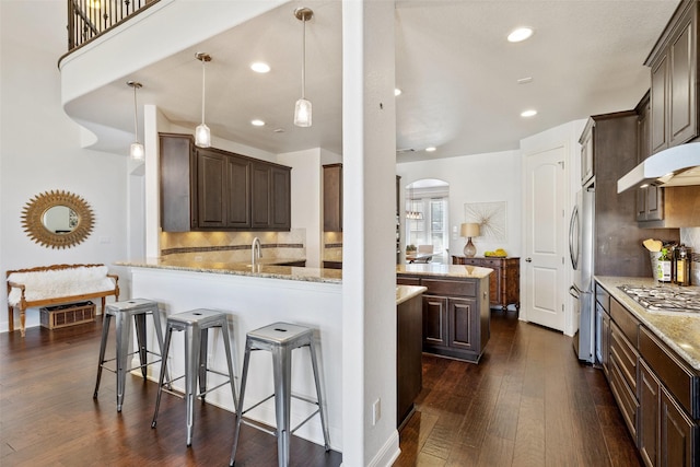 kitchen featuring light stone counters, dark hardwood / wood-style floors, decorative light fixtures, stainless steel appliances, and kitchen peninsula