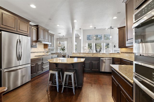 kitchen with a kitchen bar, sink, dark hardwood / wood-style floors, stainless steel appliances, and kitchen peninsula