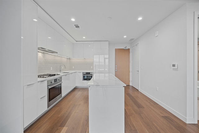 kitchen featuring sink, light hardwood / wood-style flooring, white cabinetry, stainless steel appliances, and decorative backsplash