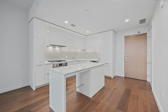 kitchen with a breakfast bar area, white cabinetry, tasteful backsplash, dark hardwood / wood-style flooring, and a kitchen island