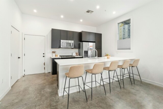 kitchen with appliances with stainless steel finishes, decorative backsplash, sink, a breakfast bar, and a center island with sink