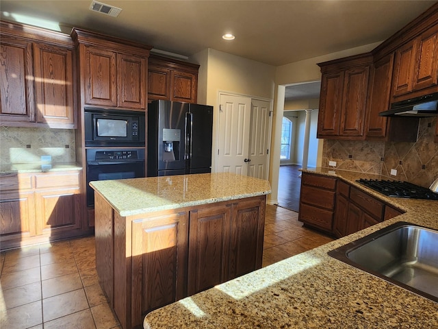 kitchen featuring backsplash, light stone counters, light tile patterned flooring, a kitchen island, and black appliances