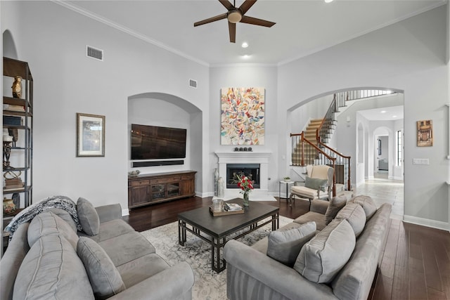 living room featuring ceiling fan, wood-type flooring, ornamental molding, and a towering ceiling