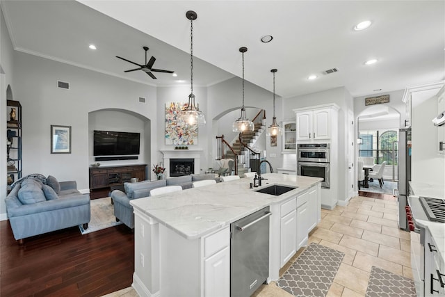 kitchen with light stone countertops, white cabinets, stainless steel appliances, sink, and a kitchen island with sink