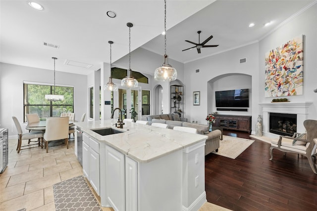 kitchen featuring white cabinets, light stone counters, a kitchen island with sink, and pendant lighting