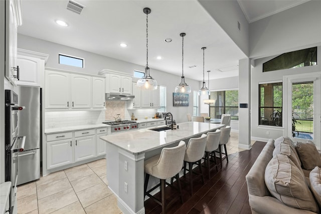 kitchen featuring hanging light fixtures, sink, white cabinetry, light stone countertops, and a center island with sink