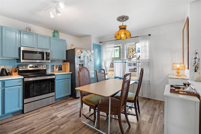 kitchen with hanging light fixtures, light wood-type flooring, stainless steel appliances, and blue cabinets