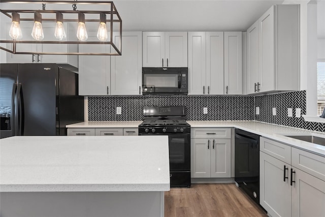 kitchen featuring backsplash, black appliances, light hardwood / wood-style flooring, and hanging light fixtures