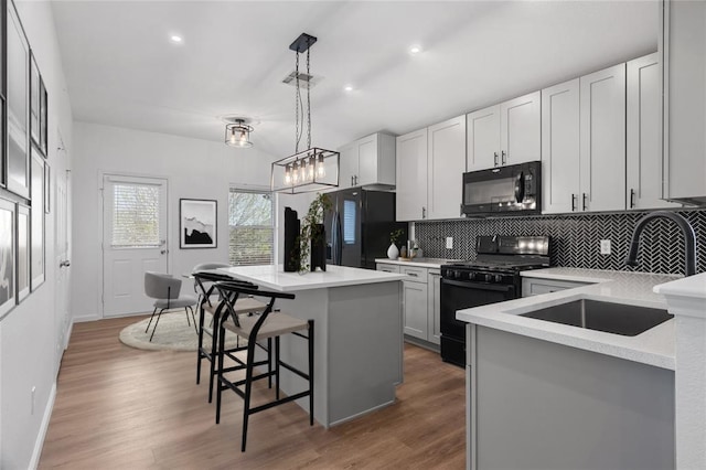 kitchen featuring tasteful backsplash, a center island, a breakfast bar area, black appliances, and a sink