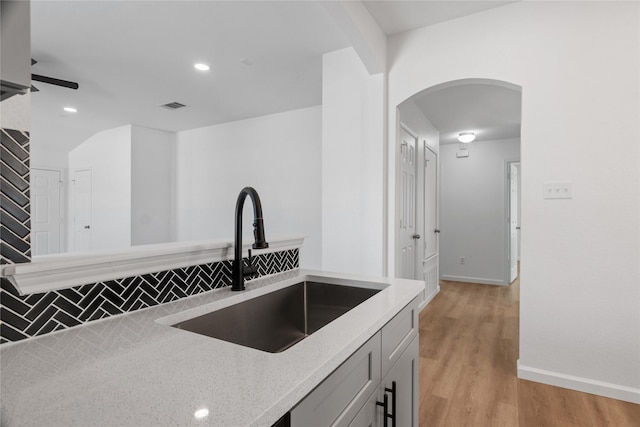 kitchen with light hardwood / wood-style flooring, ceiling fan, sink, backsplash, and light stone countertops