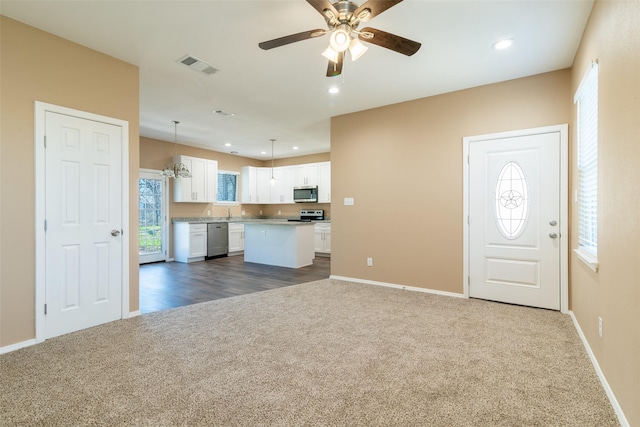 kitchen featuring dark carpet, white cabinets, a kitchen island, decorative light fixtures, and stainless steel appliances