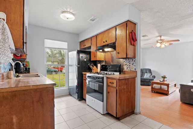 kitchen with a textured ceiling, tasteful backsplash, light tile patterned floors, sink, and gas range gas stove