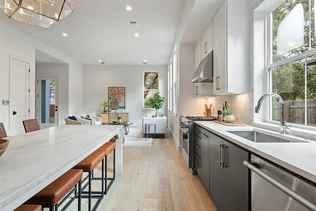 kitchen with a kitchen bar, under cabinet range hood, backsplash, a sink, and appliances with stainless steel finishes