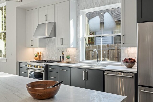 kitchen featuring a sink, range hood, stainless steel appliances, white cabinets, and decorative backsplash