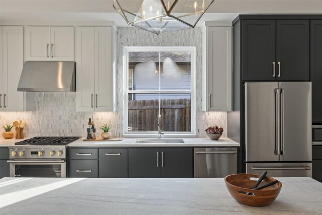 kitchen featuring under cabinet range hood, backsplash, a sink, high end appliances, and a notable chandelier