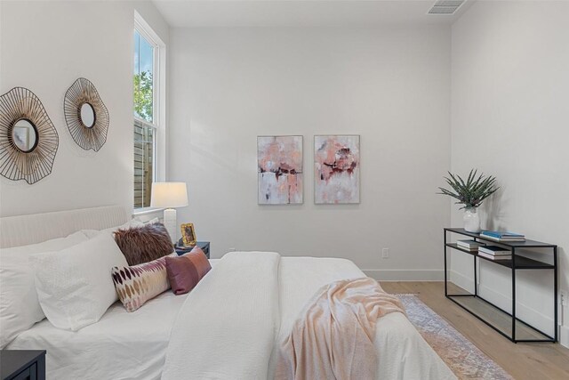 bedroom with baseboards, visible vents, and wood finished floors