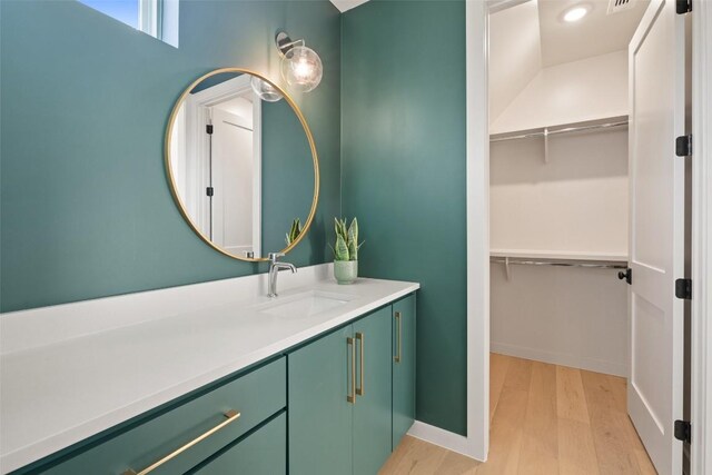 bathroom with baseboards, a walk in closet, wood finished floors, and vanity