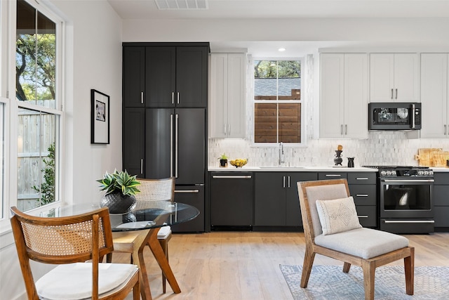 kitchen with tasteful backsplash, light countertops, white cabinetry, a sink, and black appliances