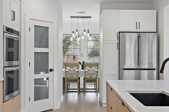 kitchen with sink, appliances with stainless steel finishes, light stone counters, white cabinets, and decorative light fixtures