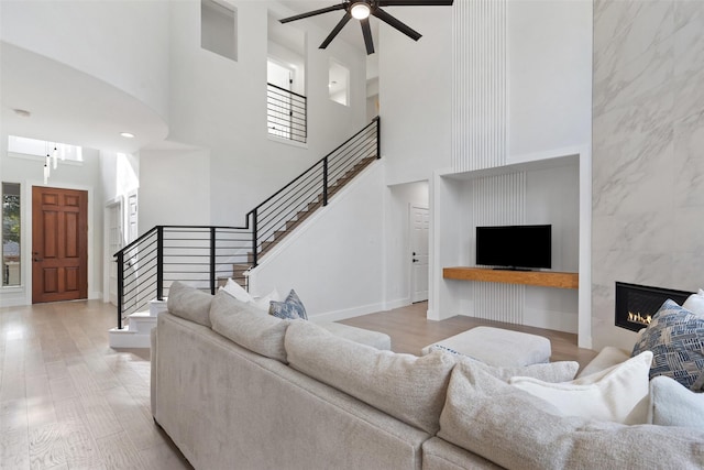 living room with a towering ceiling, a high end fireplace, light hardwood / wood-style floors, and ceiling fan