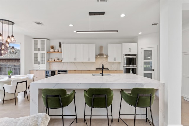 kitchen with a breakfast bar, white cabinetry, hanging light fixtures, stainless steel double oven, and wall chimney exhaust hood