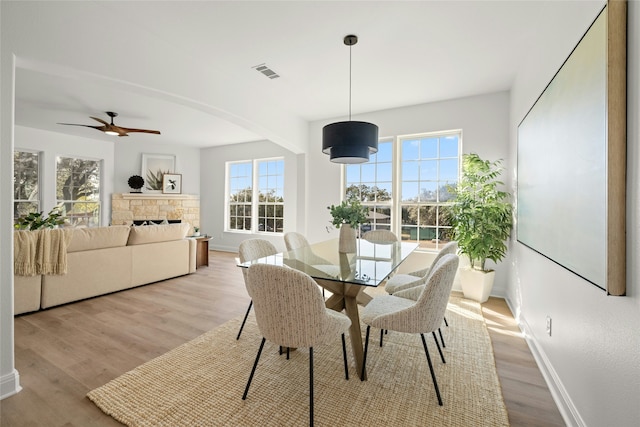 dining room featuring light hardwood / wood-style floors, ceiling fan, and a fireplace