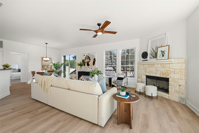 living room with light hardwood / wood-style floors, a stone fireplace, and ceiling fan with notable chandelier