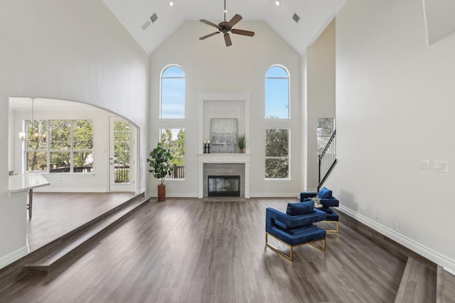 unfurnished living room featuring ceiling fan with notable chandelier, a towering ceiling, and dark hardwood / wood-style flooring