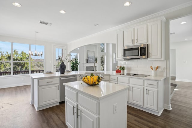 kitchen with kitchen peninsula, backsplash, white cabinetry, a kitchen island, and stainless steel appliances