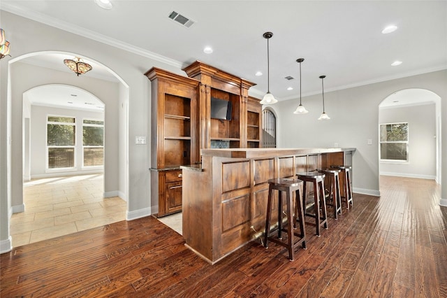 bar with pendant lighting, dark wood-type flooring, a wealth of natural light, and ornamental molding