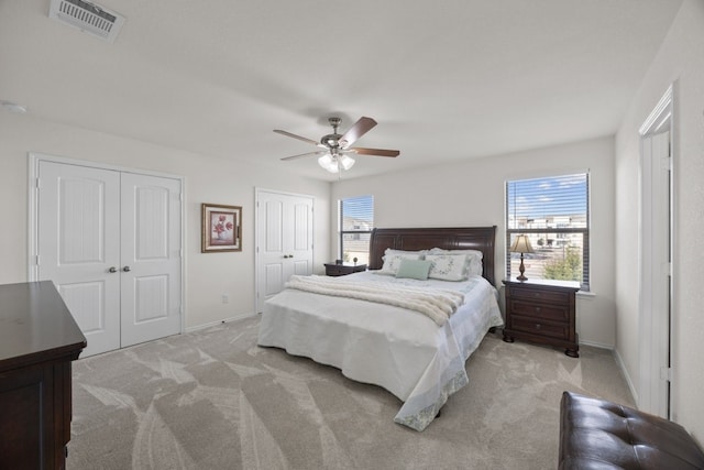 bedroom with ceiling fan, two closets, and light carpet